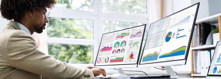business man looking at statistics on two computer monitors in a home office