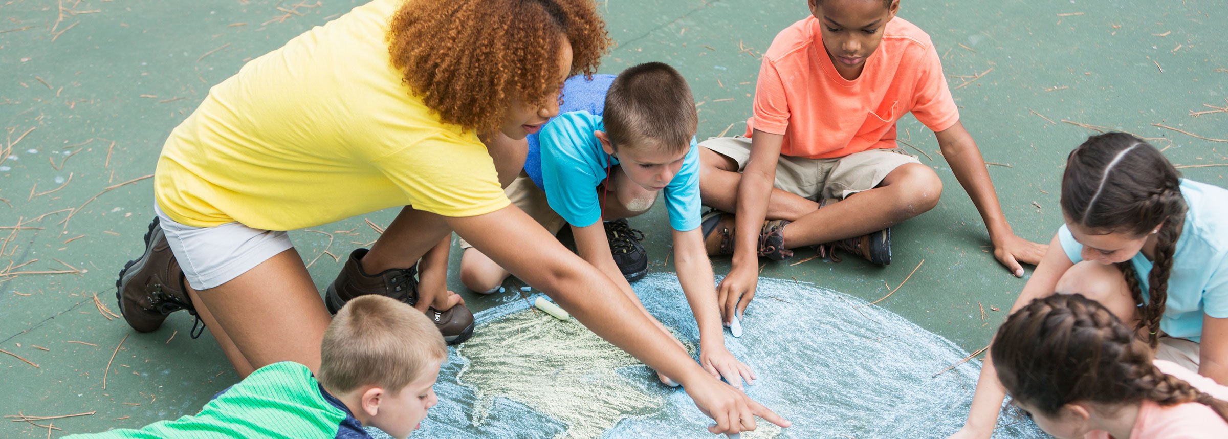 teacher helping young children draw a map in chalk on the ground