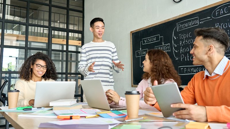 Multiracial young professional business startup gen z team students group working on project listen to Asian leader in contemporary office classroom with gadgets.