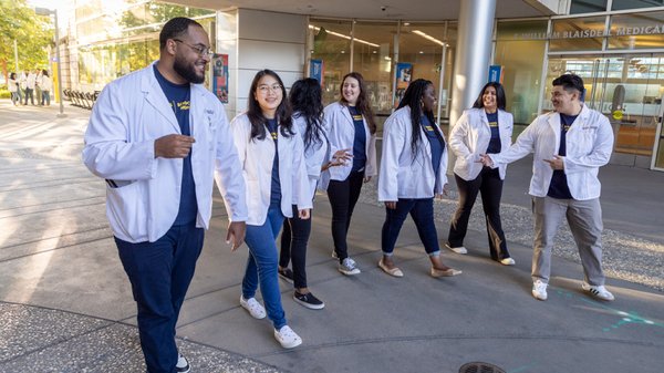 medical students in white coats walking together on a university campus.